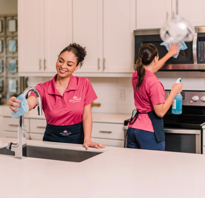 A pair of Molly Maid professionals is cleaning a kitchen.